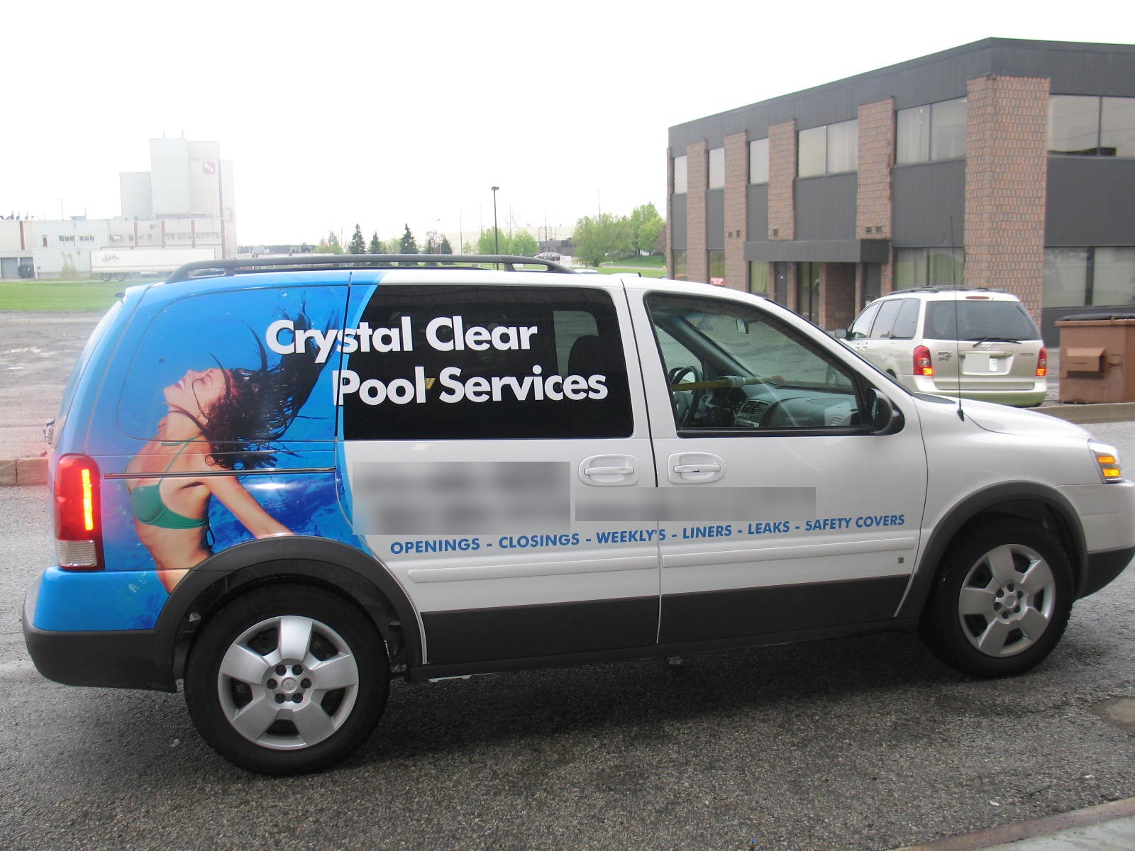 Side view of a minivan with a printed wrap and lettering, parked in a lot